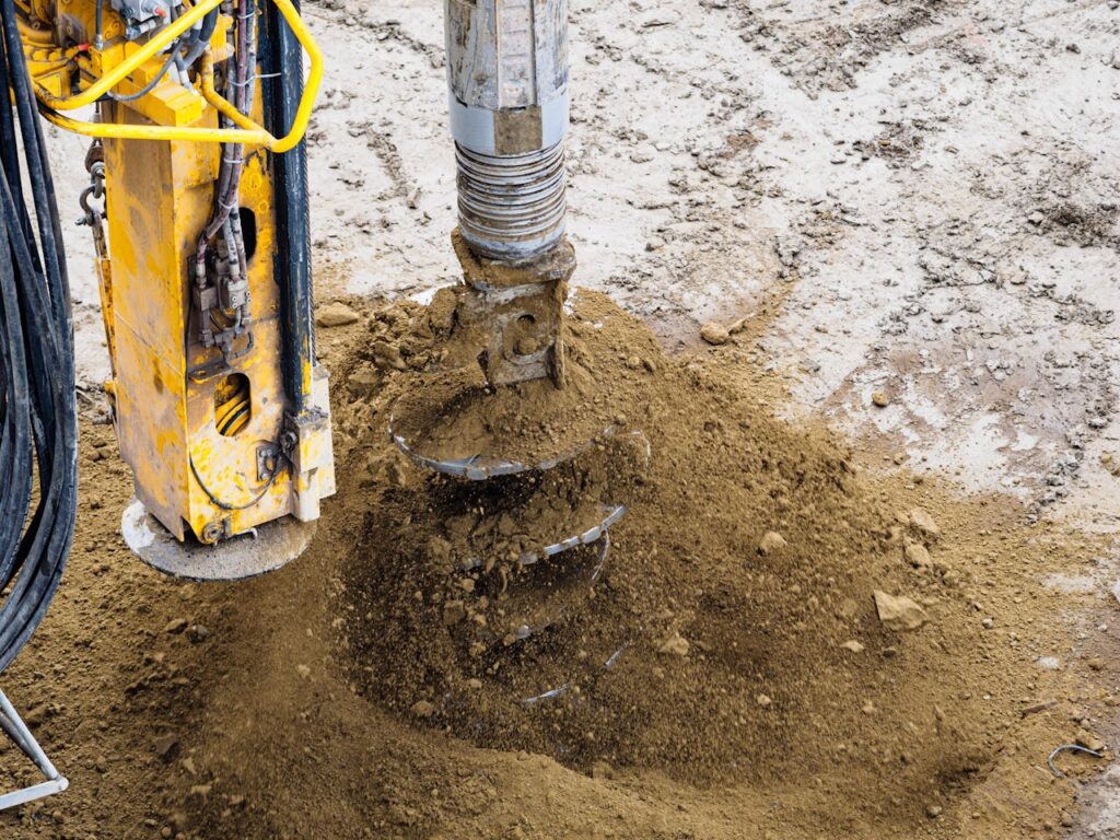A close-up of a powerful drilling machine working on soil at a construction site.